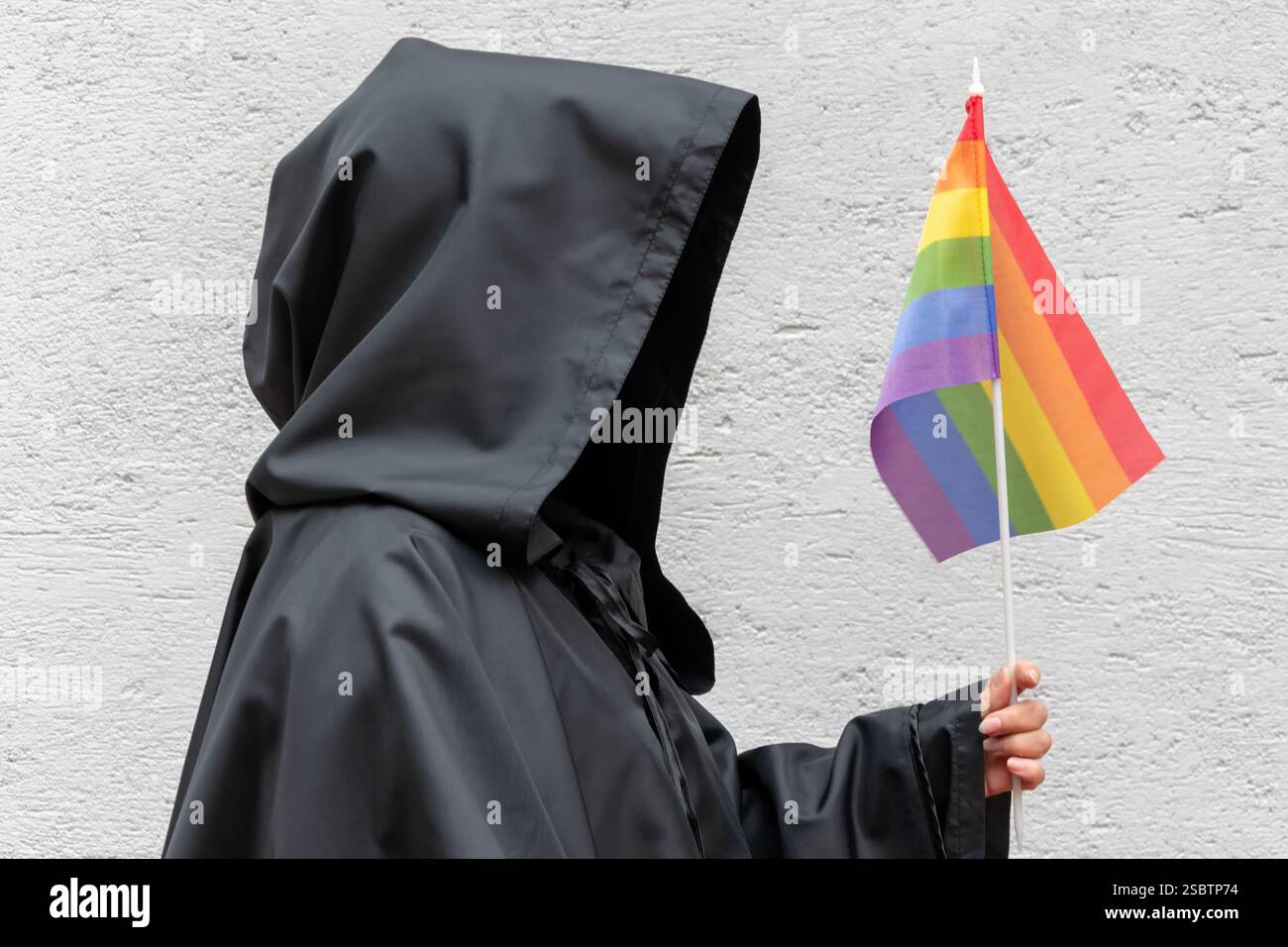 Un uomo con una felpa con cappuccio nera ha una bandiera arcobaleno LGBT Foto Stock
