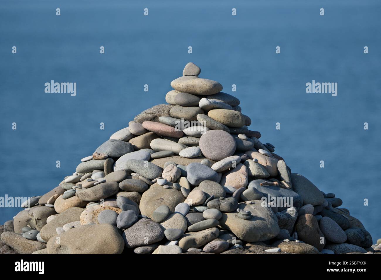Piramide di ciottoli di fronte al mare con sfondo blu del cielo. Piramide di pietre sulla riva del mare contro il cielo blu. Zen e concetto di armonia. Foto Stock