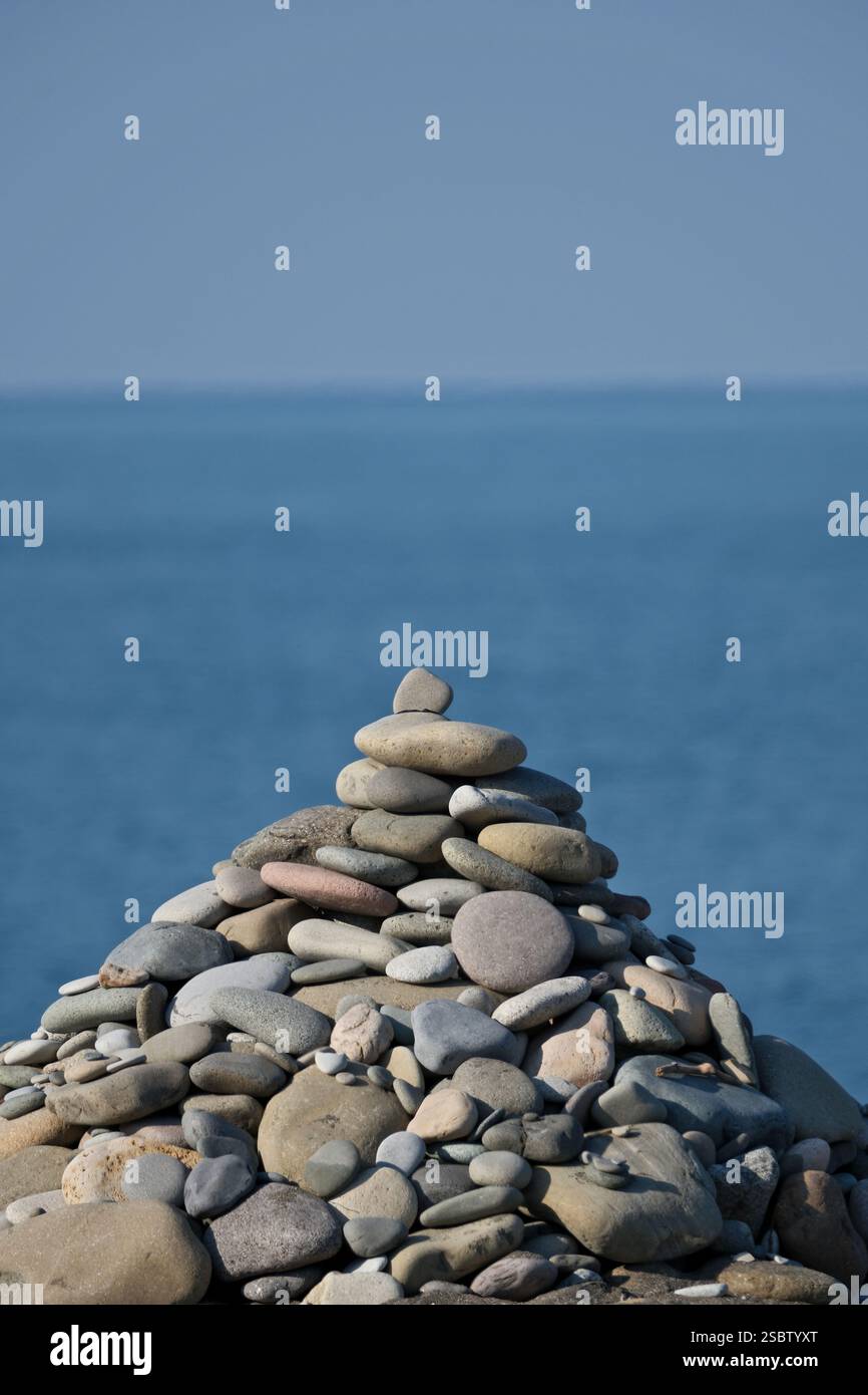Piramide di ciottoli di fronte al mare con sfondo blu del cielo. Piramide di pietre sulla riva del mare contro il cielo blu. Zen e concetto di armonia. Foto Stock