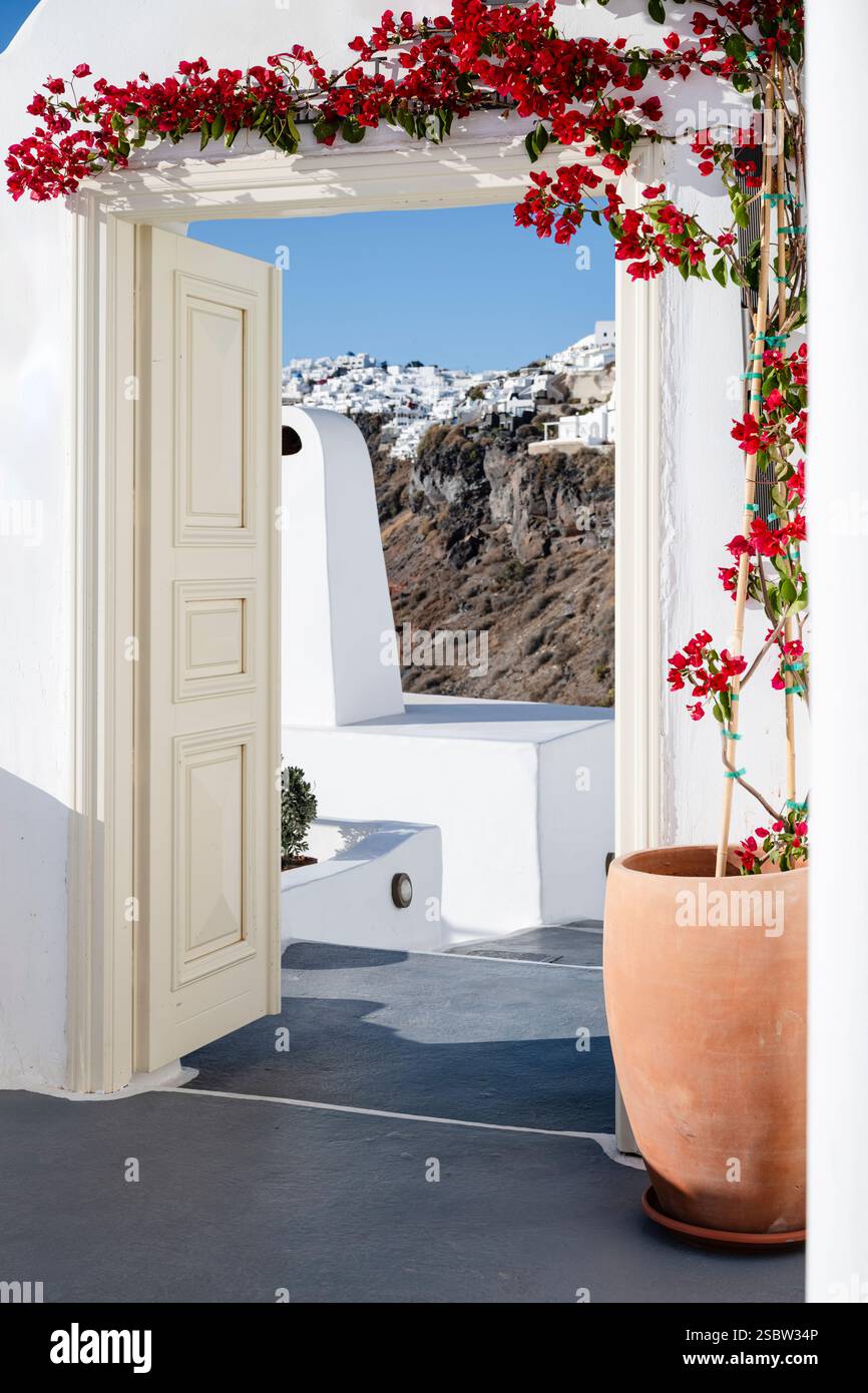 Vista delle scogliere di Santorini e del sole attraverso un arco con una porta aperta e bouganville fiorite, Cicladi, Grecia Foto Stock