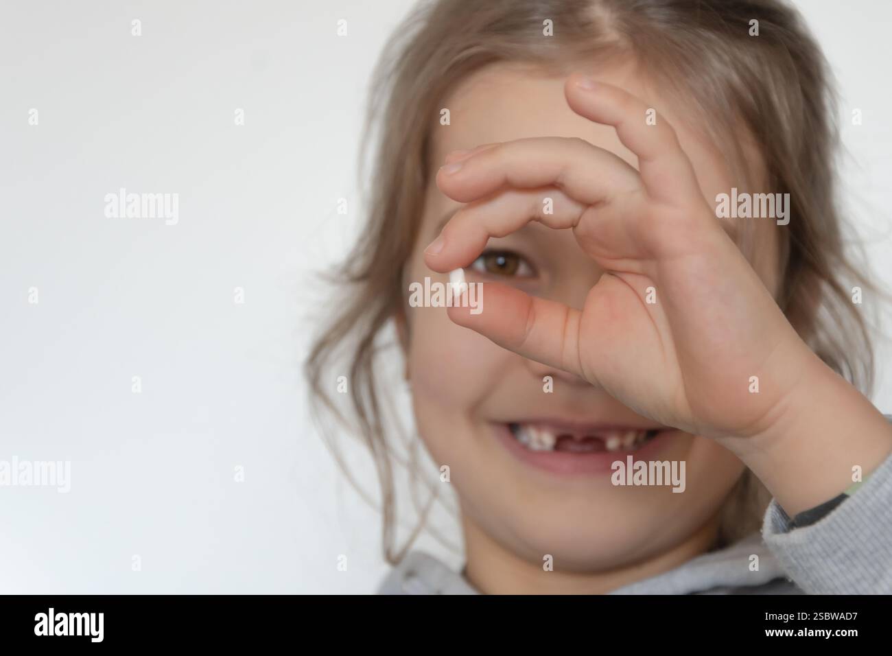 La ragazza dai denti spalancati regge il suo dente del bambino e sorride Foto Stock