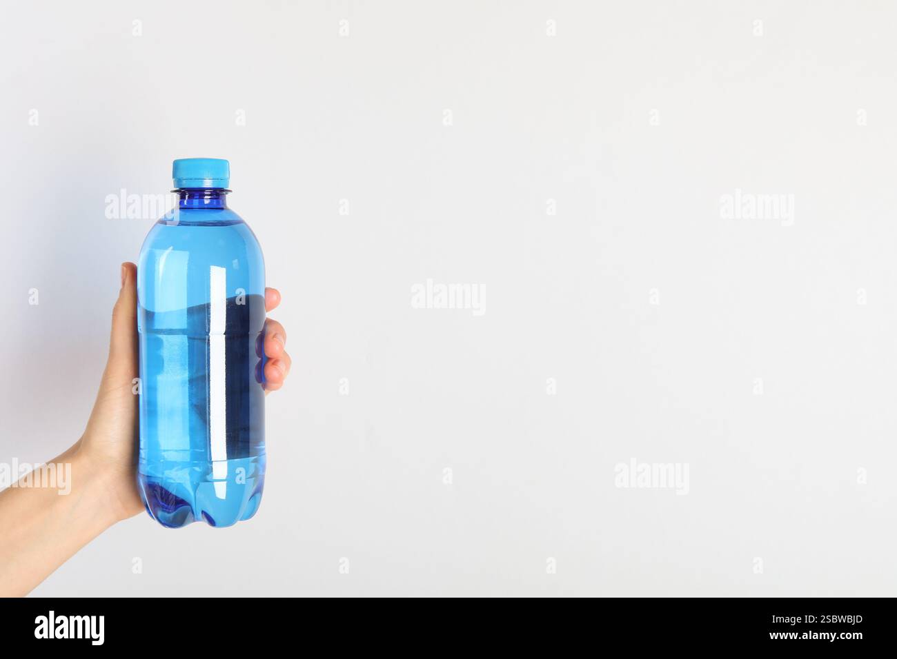 Donna che tiene in mano una bottiglia d'acqua di plastica su sfondo chiaro, primo piano. Spazio per il testo Foto Stock