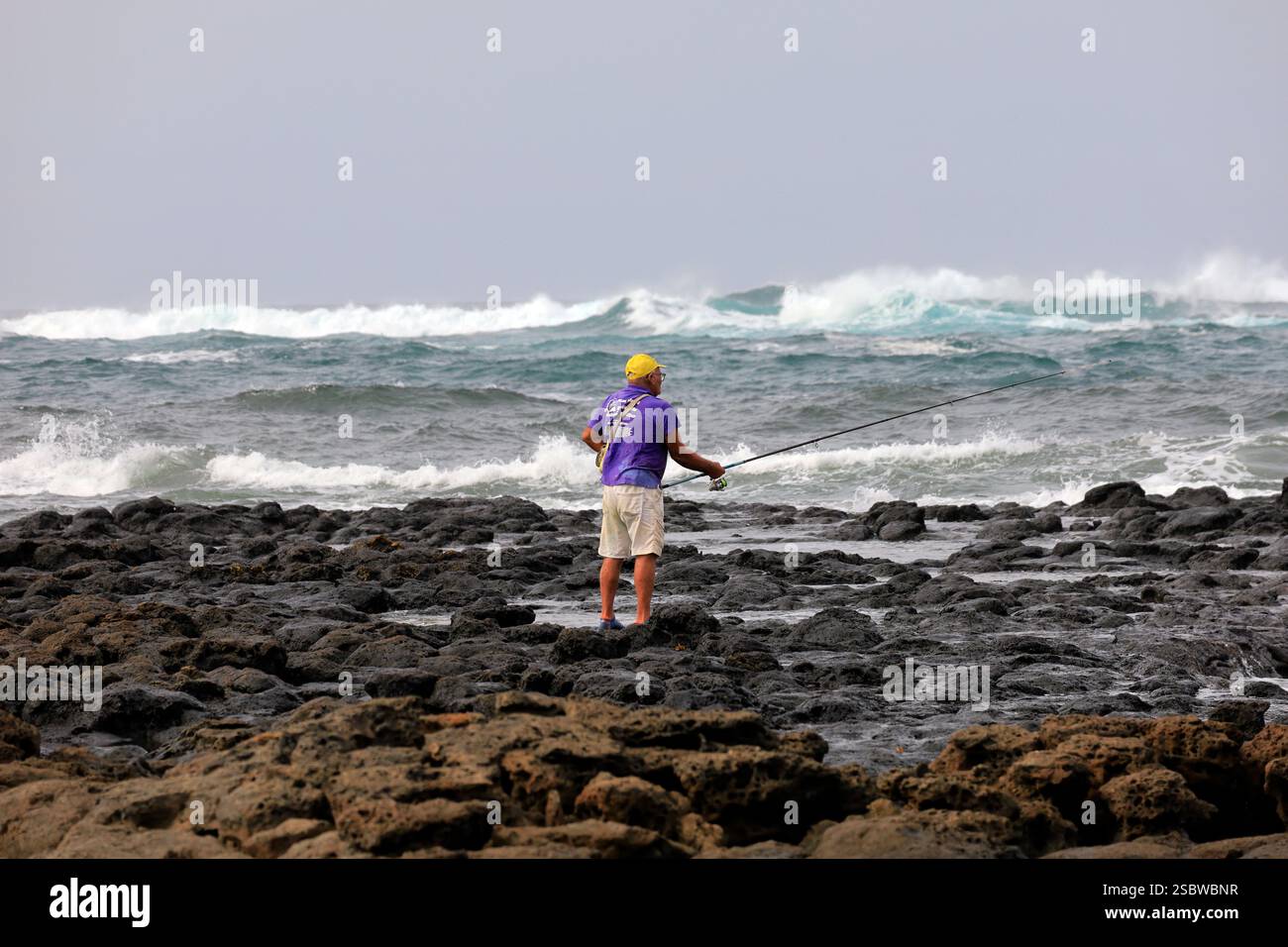 Uomo maturo solitario che pesca con canna da pesca su coste vulcaniche rocciose, Fuerteventura, Isole Canarie, Spagna. Presa novembre 2024 Foto Stock
