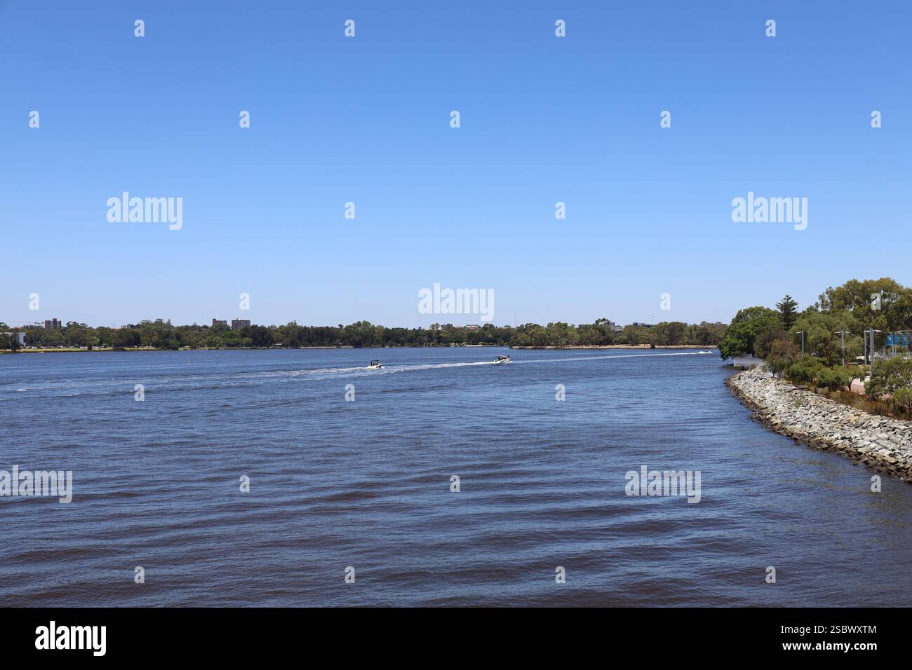 panorama panoramico con ampio angolo acque blu profonde di un ampio fiume e argini rocciose rinforzate in un ambiente urbano sotto cieli blu profondi e privi di nuvole Foto Stock