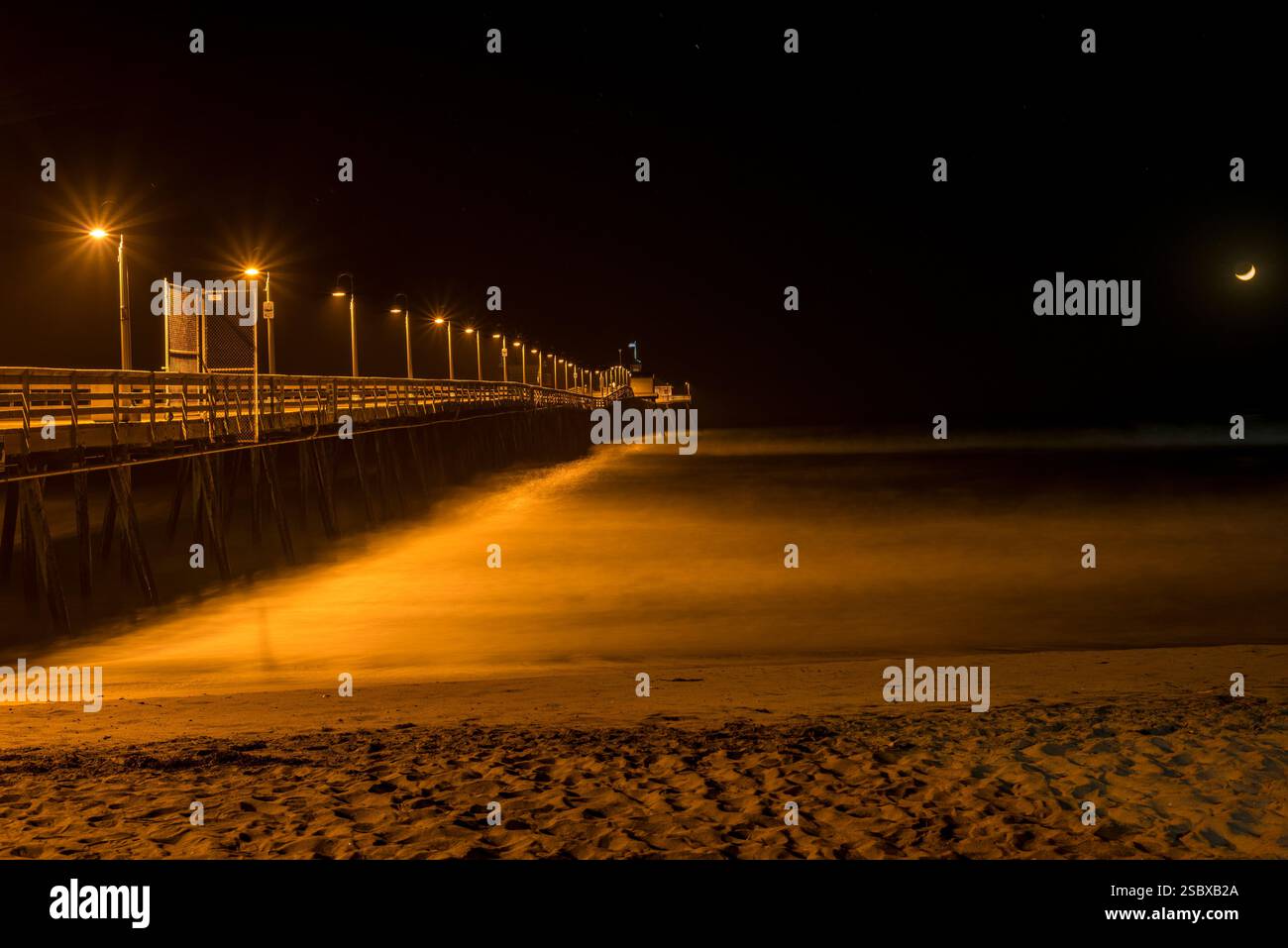 Vista notturna di un molo illuminato dalle luci sulle calme acque del mare Foto Stock