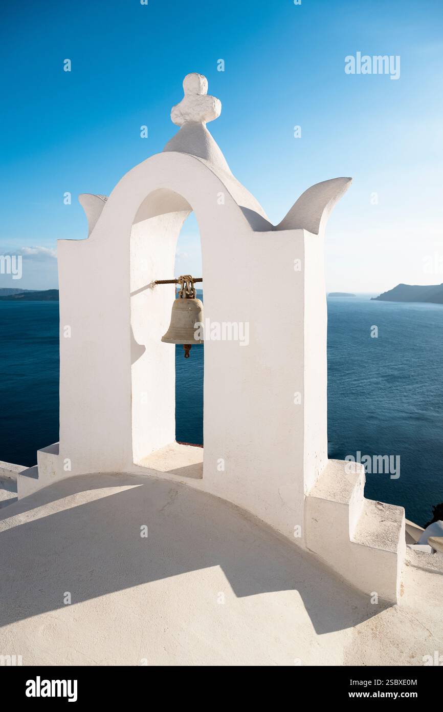 Campana nel campanile bianco di una cappella a Oia di fronte alla caldera di Santorini contro un cielo blu, Grecia Foto Stock