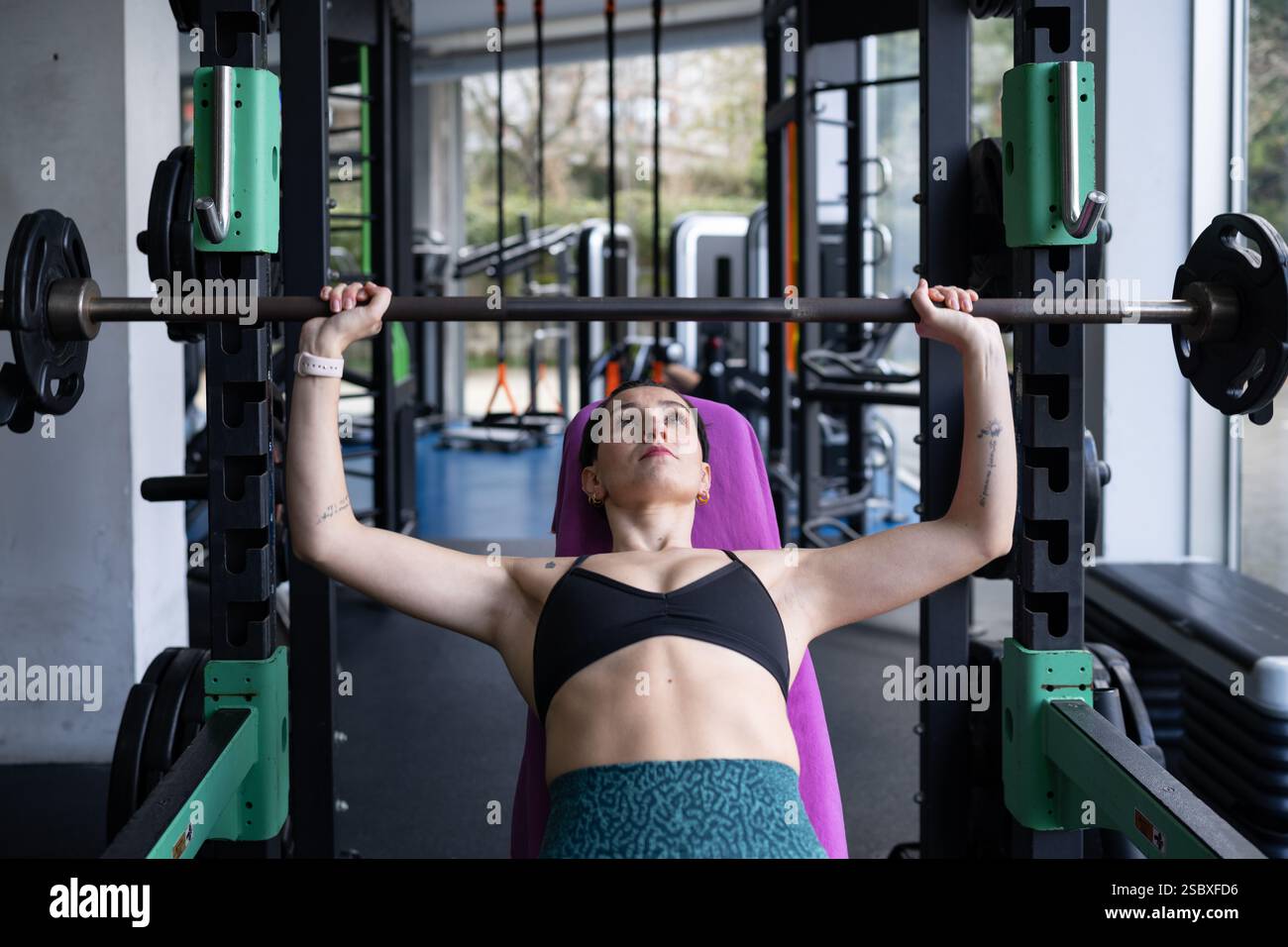 Giovane donna impegnata in esercizi di panchina con un barbell, dimostrando forza e dedizione costante agli obiettivi di fitness all'interno di un g contemporaneo Foto Stock