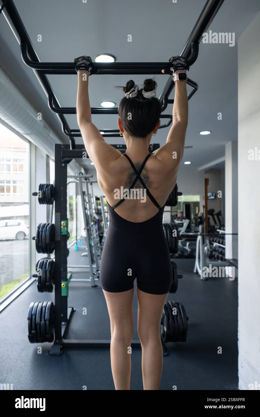Un atleta determinato dimostra forza e dedizione mentre esegue tiri su un bar in una palestra moderna, mostrando il percorso stimolante di Fitne Foto Stock