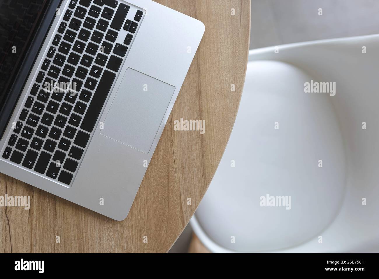 Vista dall'alto di un computer portatile su un tavolo in legno accanto a una sedia bianca, stile minimalista dello spazio di lavoro Foto Stock