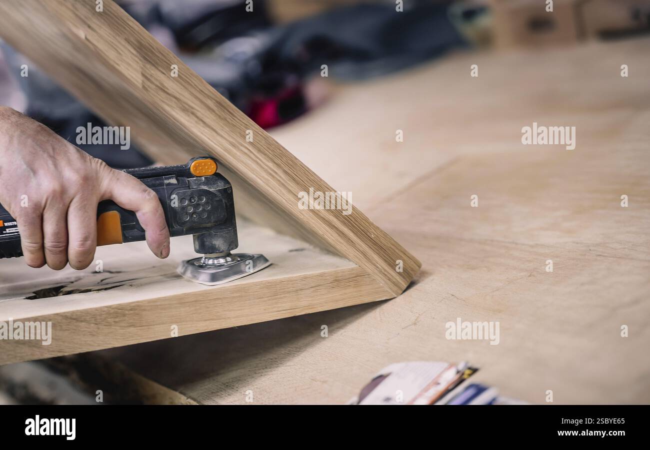 Una mano che utilizza una levigatrice su un pezzo di legno in un'officina, concentrandosi sulla levigatura della superficie Foto Stock