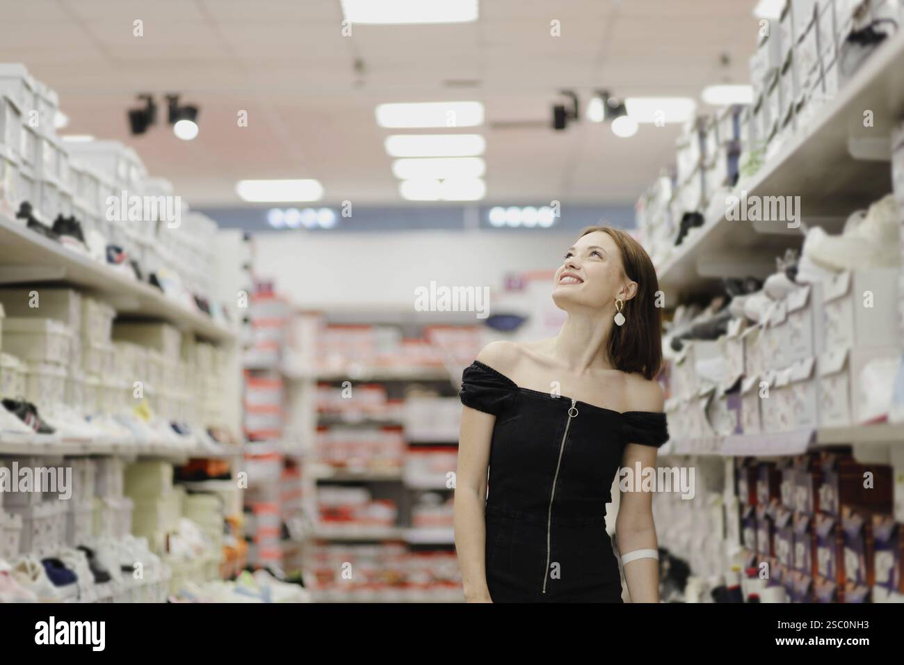 Una donna con un abito nero guarda verso l'alto in un corridoio di un negozio rivestito di scatole per scarpe Foto Stock