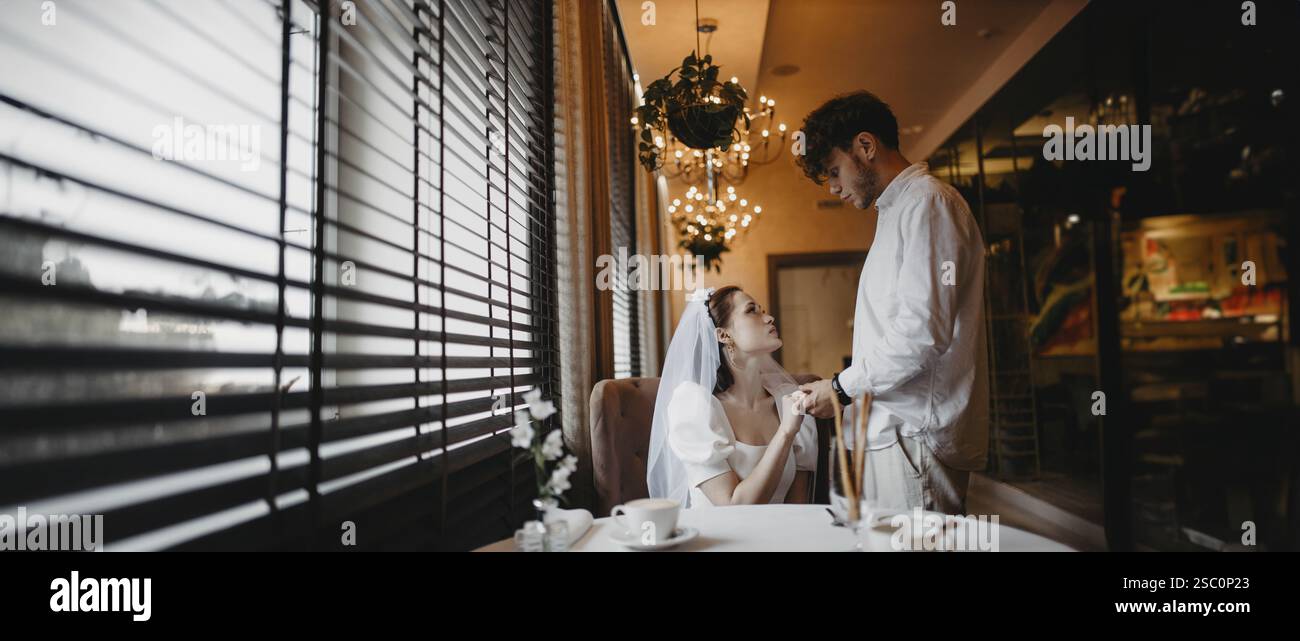 Sposo e sposo che condividono un momento romantico vicino alla finestra in un caffè con luce soffusa Foto Stock
