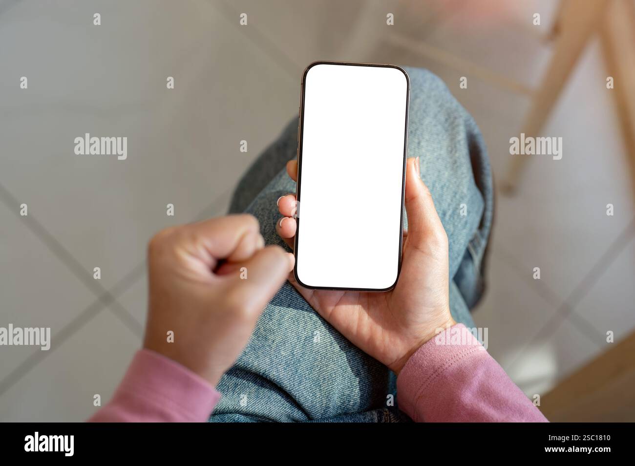 Primo piano di una donna frustrata in jeans seduti al chiuso, stringendosi il pugno mentre usa lo smartphone. uno smartphone con un modello con schermo bianco Foto Stock