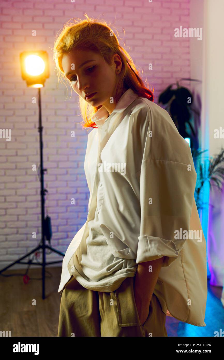 Un giovane in uno studio artistico con illuminazione colorata mette in mostra uno stile di moda moderno durante una sessione creativa Foto Stock