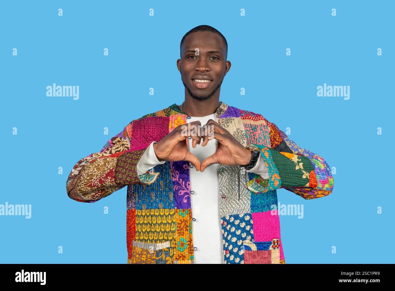 Uomo elegante che forma il cuore con le mani, esprimendo amore e positività su uno sfondo blu brillante Foto Stock