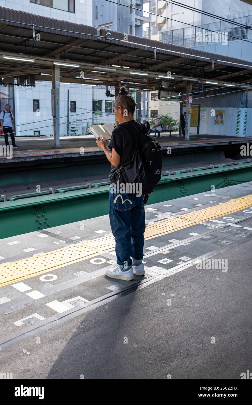 Hip Young Woman che legge sul binario dei treni alla stazione Nakano di Tokyo in Giappone Foto Stock