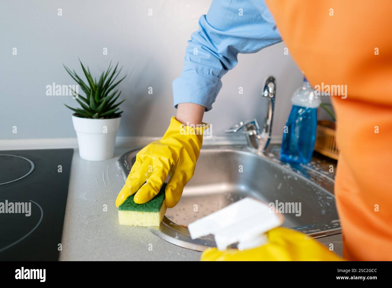 Ogni giorno inizia con la pulizia. La donna utilizza un detergente ad azione rapida per lavare il lavandino e creare un'atmosfera accogliente in cucina. Foto Stock