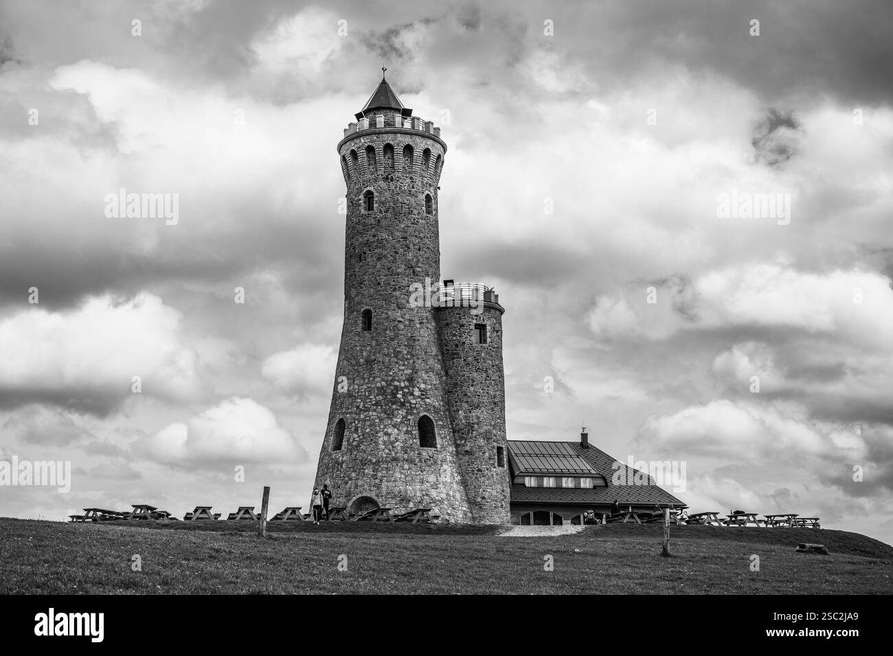 La Dalimil Lookout Tower si erge alta sulla collina di Vetrov, mostrando la sua architettura in pietra sotto un suggestivo cielo nuvoloso in Cechia. I visitatori esplorano l'area vicino alla base della torre. Foto Stock