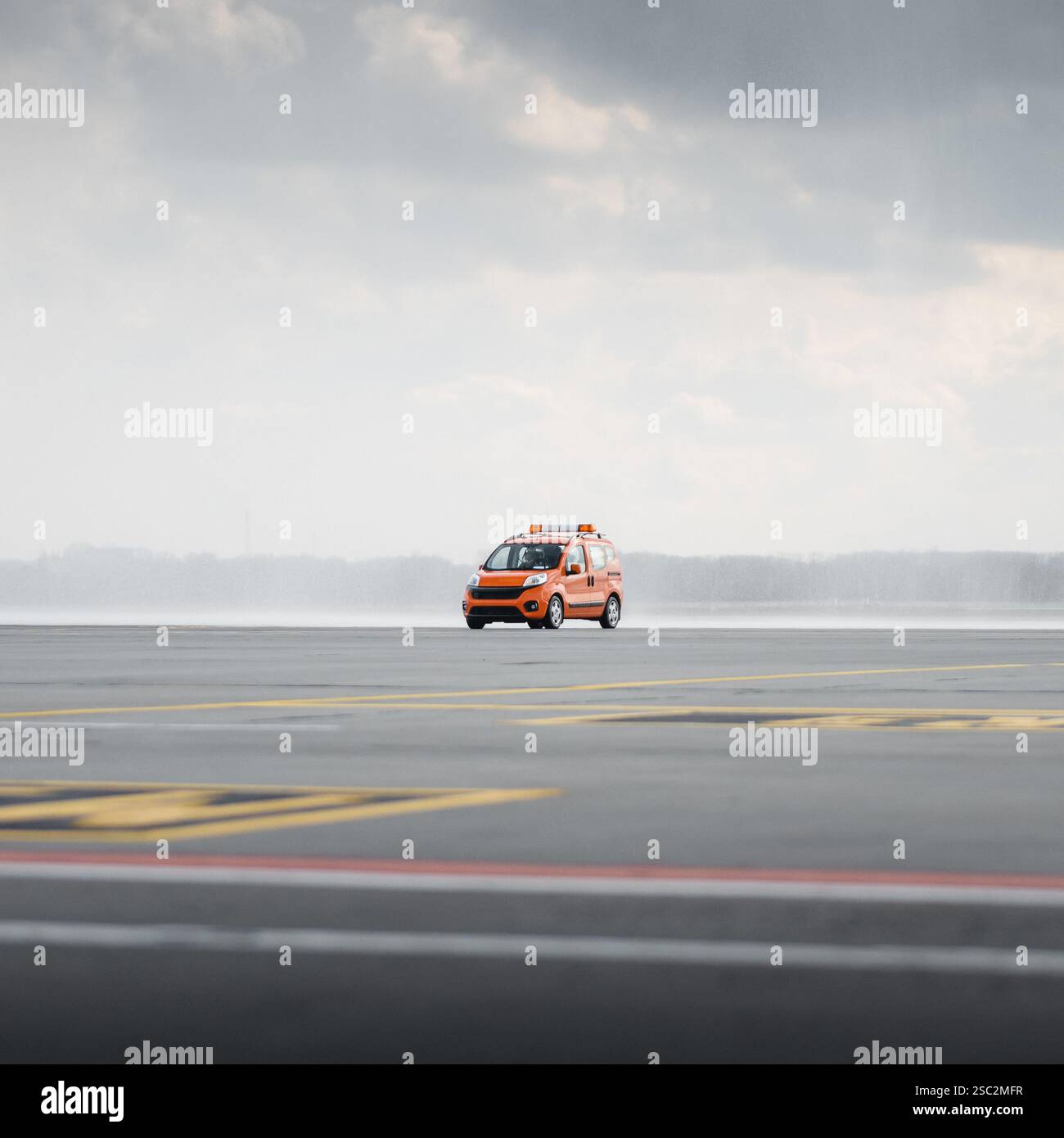 Auto arancione che mi segue all'aeroporto. Piccolo furgone con luci lampeggianti color ambra che attraversa il piazzale dell'aeroporto e guida un aereo. Nuvole piovose sullo sfondo Foto Stock