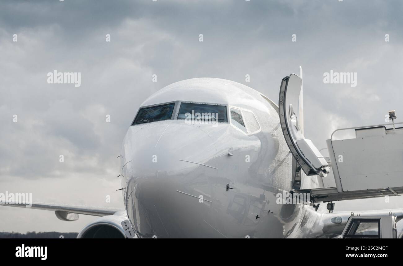 Vista ravvicinata della parte anteriore dell'aereo bianco con la scala d'imbarco dei passeggeri attaccata. Aereo con porta aperta e cielo nuvoloso sullo sfondo. Foto Stock Vista ravvicinata della parte anteriore dell'aereo bianco con la scala d'imbarco dei passeggeri attaccata. Aereo con porta aperta e cielo nuvoloso sullo sfondo. Foto Stock