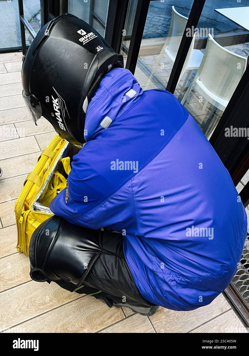 Kiev, Ucraina - 4 febbraio 2025: Consegna Glovo attrezzature organizzative professionali all'interno di un bar, indossando casco di sicurezza e attrezzatura. Foto Stock