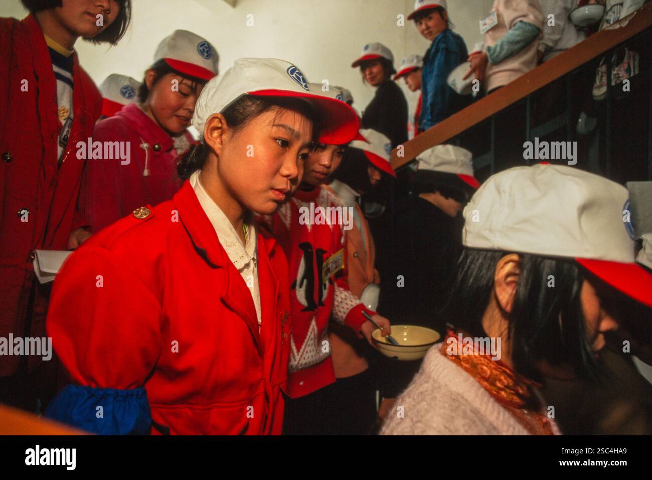 Un gruppo di giovani donne operaie della fabbrica di scarpe sulle scale che vanno per la pausa pranzo indossando abiti rossi e berretti bianchi con logo. Foto Stock