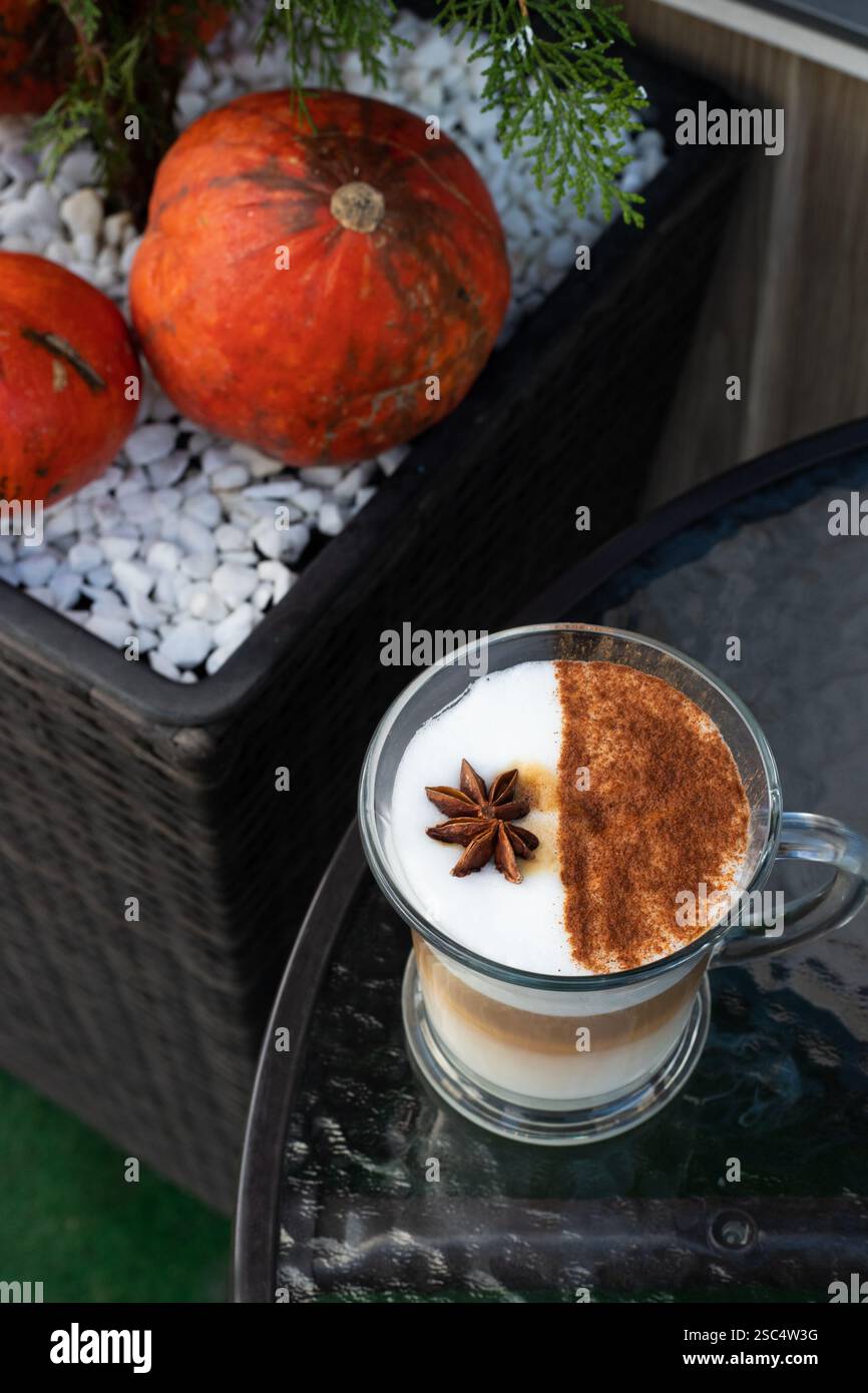 Latte autunnale con cannella e anice stellato su un tavolo di vetro. Intimo concetto autunnale con decorazioni di zucca sullo sfondo. Foto Stock