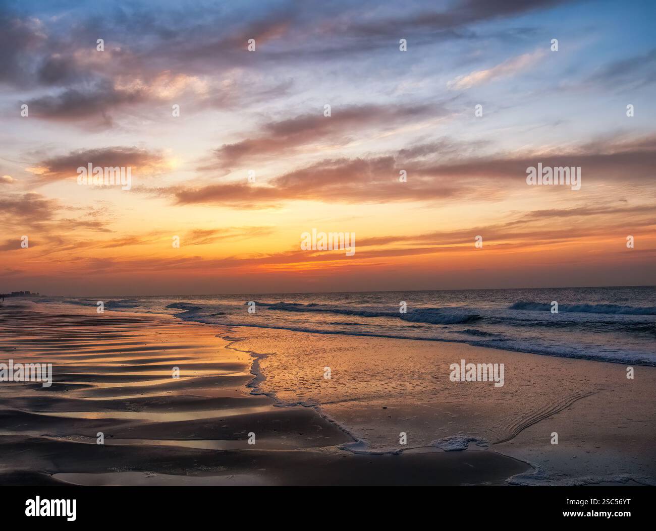 Una serena alba su una spiaggia costiera con onde dolci e riflessi dorati sulla sabbia, creando un tranquillo e tranquillo paesaggio oceanico. Foto Stock