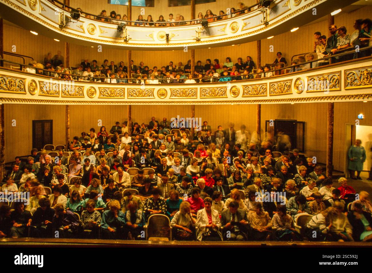 Un pubblico seduto all'interno di un teatro a Vienna, Austria, con balconi ornati e interni dettagliati. Foto Stock