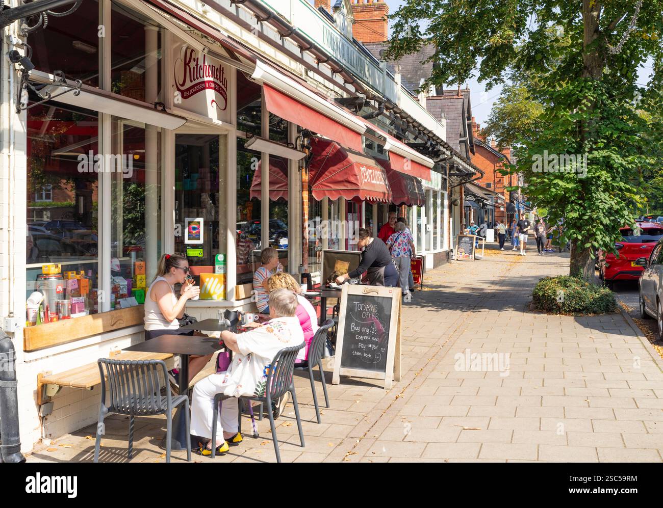 Woodhall Spa Shops - The Broadway nel centro della città con persone sedute fuori dalla caffetteria Kitchenetta Woodhall Spa Lincolnshire Inghilterra Regno Unito GB Europa Foto Stock