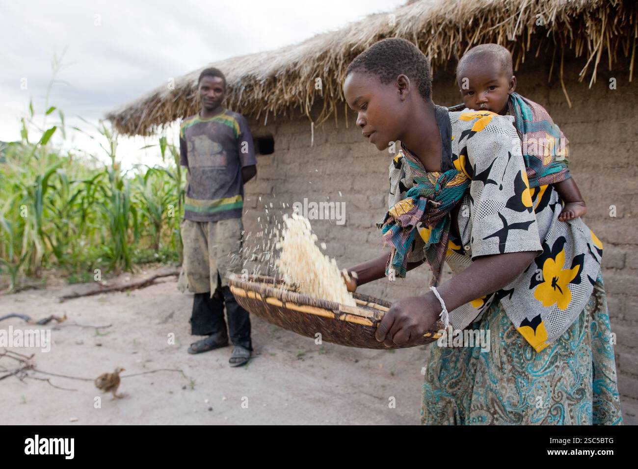 MAKEFU VILLAGE, IDODI DIVISION, TANZANIA, maggio 2008: Catherine Msigwa, 20 anni, porta il suo figlio di 6 mesi Pendo mentre inghiottisce il mais mentre suo marito Simon Oboaba, 25 anni, si trova accanto alla loro piccola casa. Foto Stock