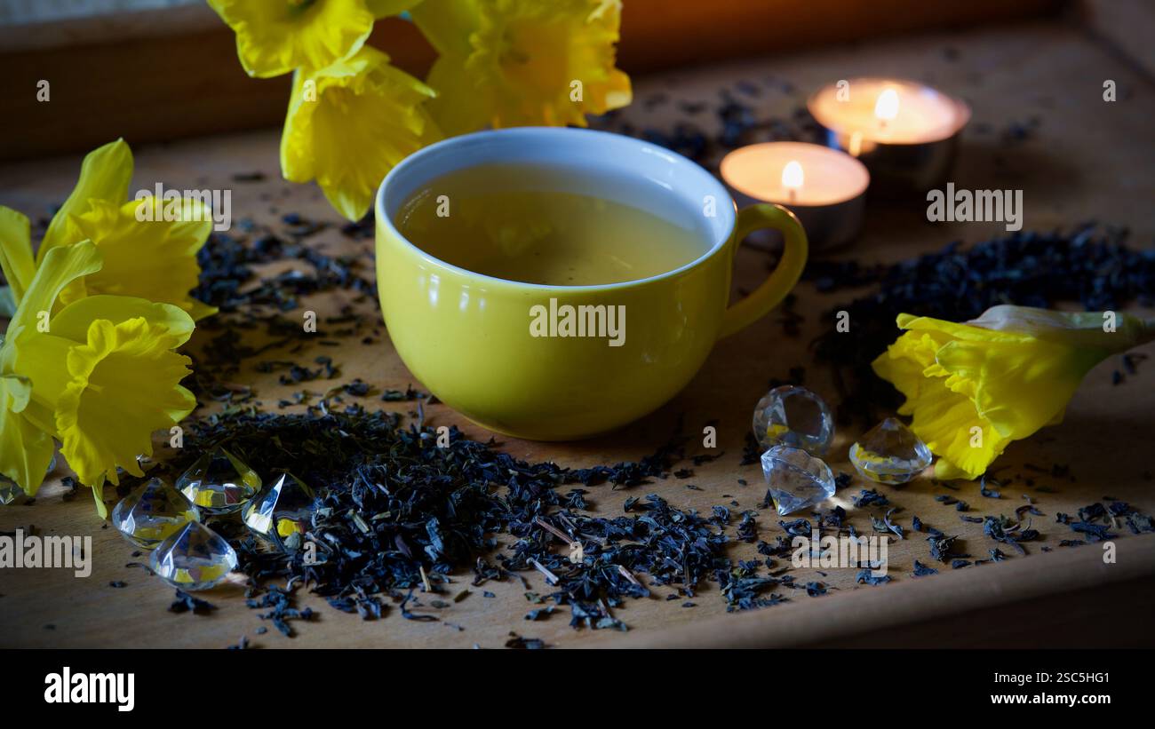 Una tazza da tè gialla, foglie di tè, narcisi, luci da tè. Foto Stock