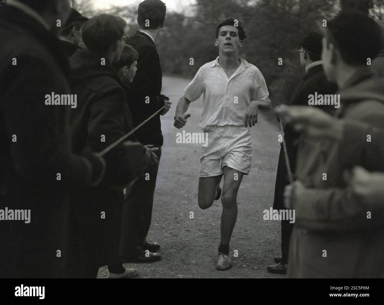 Anni '1950, storico, uno scolaro anziano che termina una gara di cross-country, con compagni in attesa che tengono la corda, Oxford, Inghilterra, Regno Unito. Foto Stock