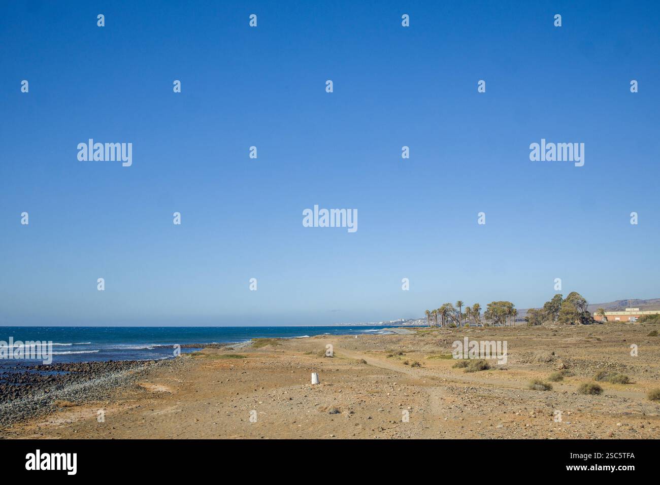 Ampia spiaggia aperta a Gran Canaria con cielo azzurro. Mix di sabbia e ciottoli sulla riva. Tranquillo e tranquillo scenario costiero. Perfetto per la spiaggia, tr Foto Stock