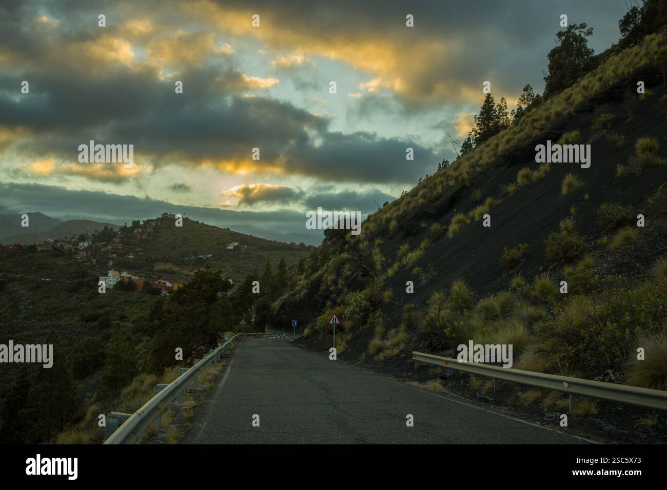 Paesaggio montuoso a Gran Canaria vicino a Bandama, con una strada tortuosa e un piccolo villaggio. Cielo spettacolare con luce calda all'alba o al tramonto. Perfetto per Foto Stock