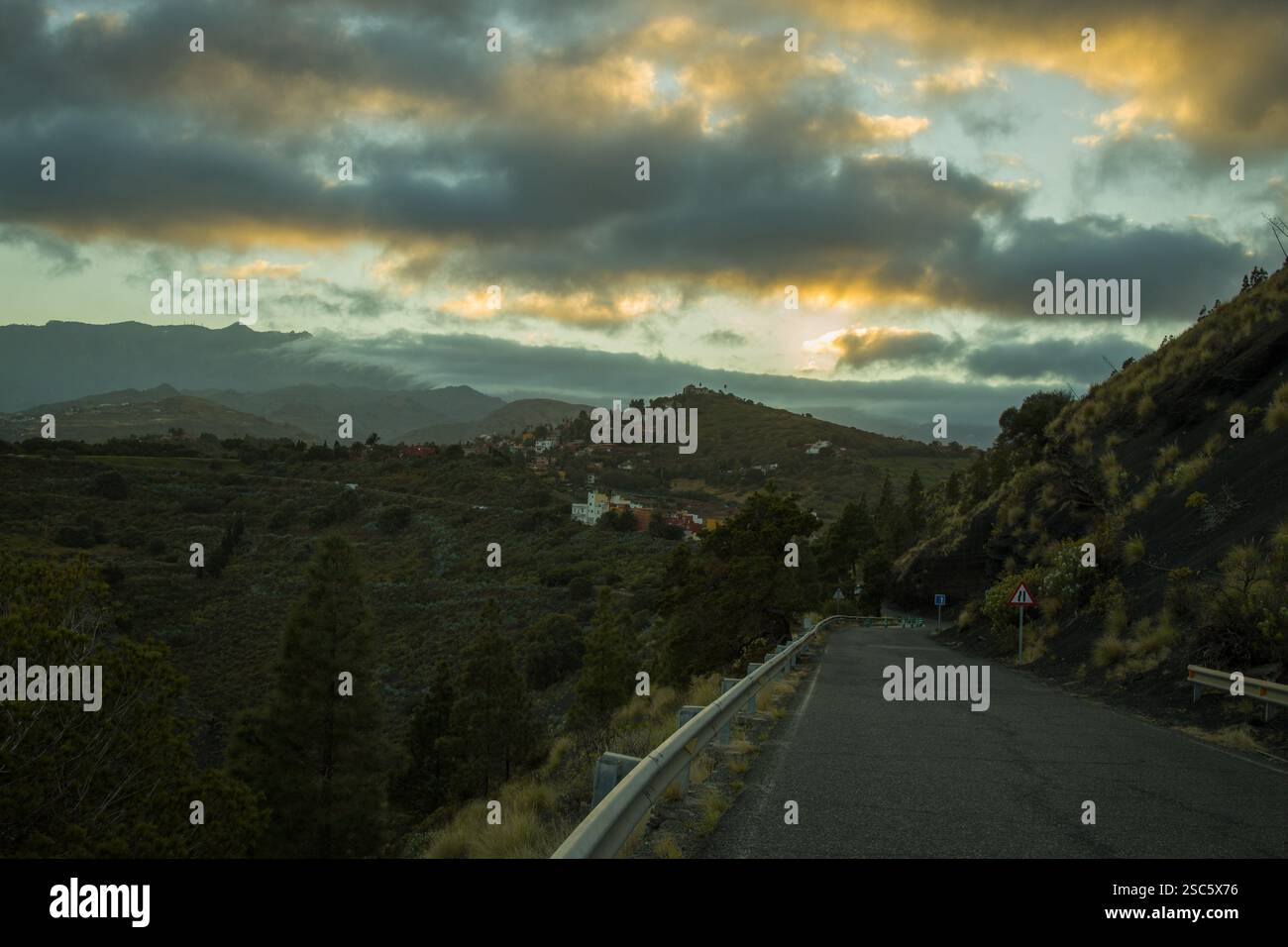 Paesaggio montuoso a Gran Canaria vicino a Bandama, con una strada tortuosa e un piccolo villaggio. Cielo spettacolare con luce calda all'alba o al tramonto. Perfetto per Foto Stock