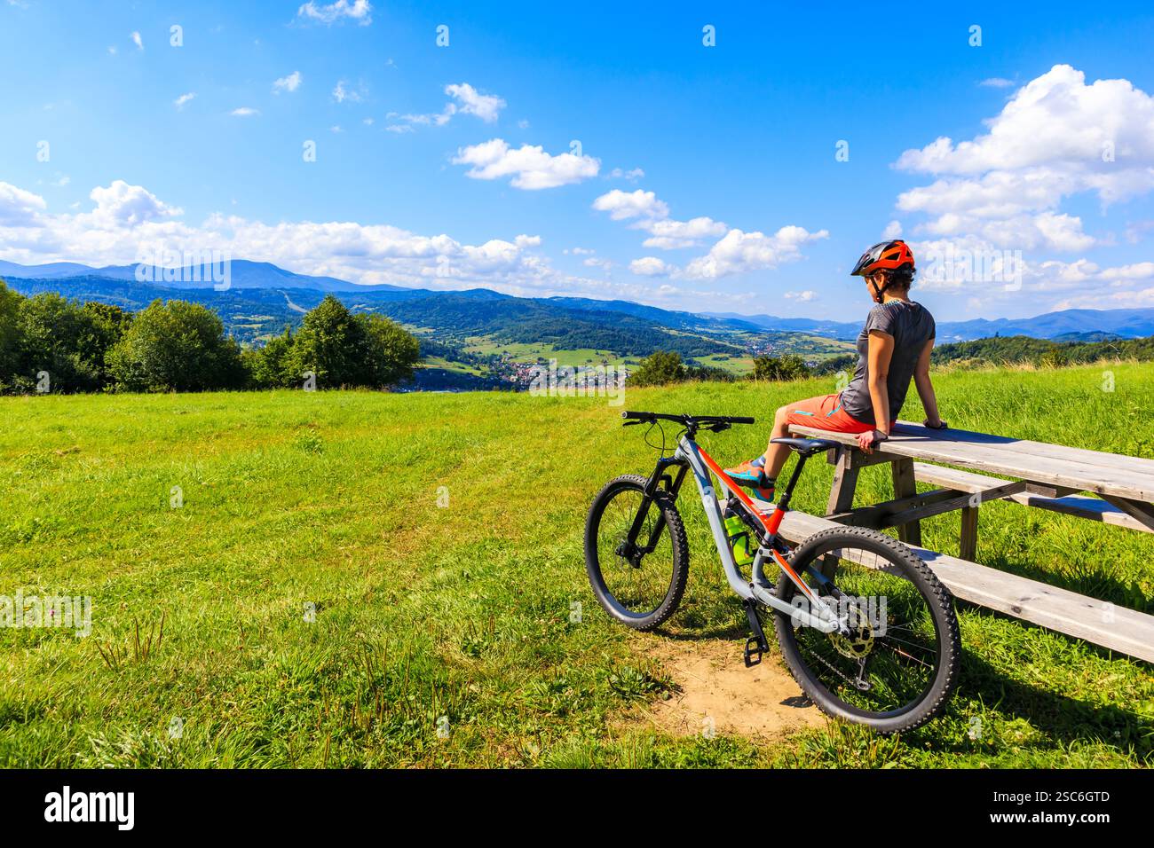Donna mountain bike seduta su un tavolo di legno sul prato verde in estate, sui monti Beskidy vicino a Zywiec, Polonia Foto Stock