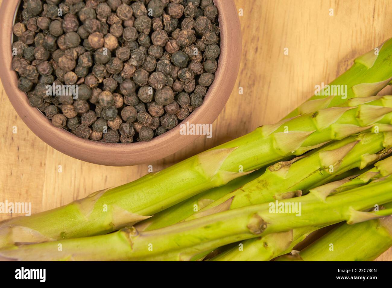 Asparagi freschi disposti su una tavola di legno con una tovaglia a scacchi blu e bianca sullo sfondo Foto Stock
