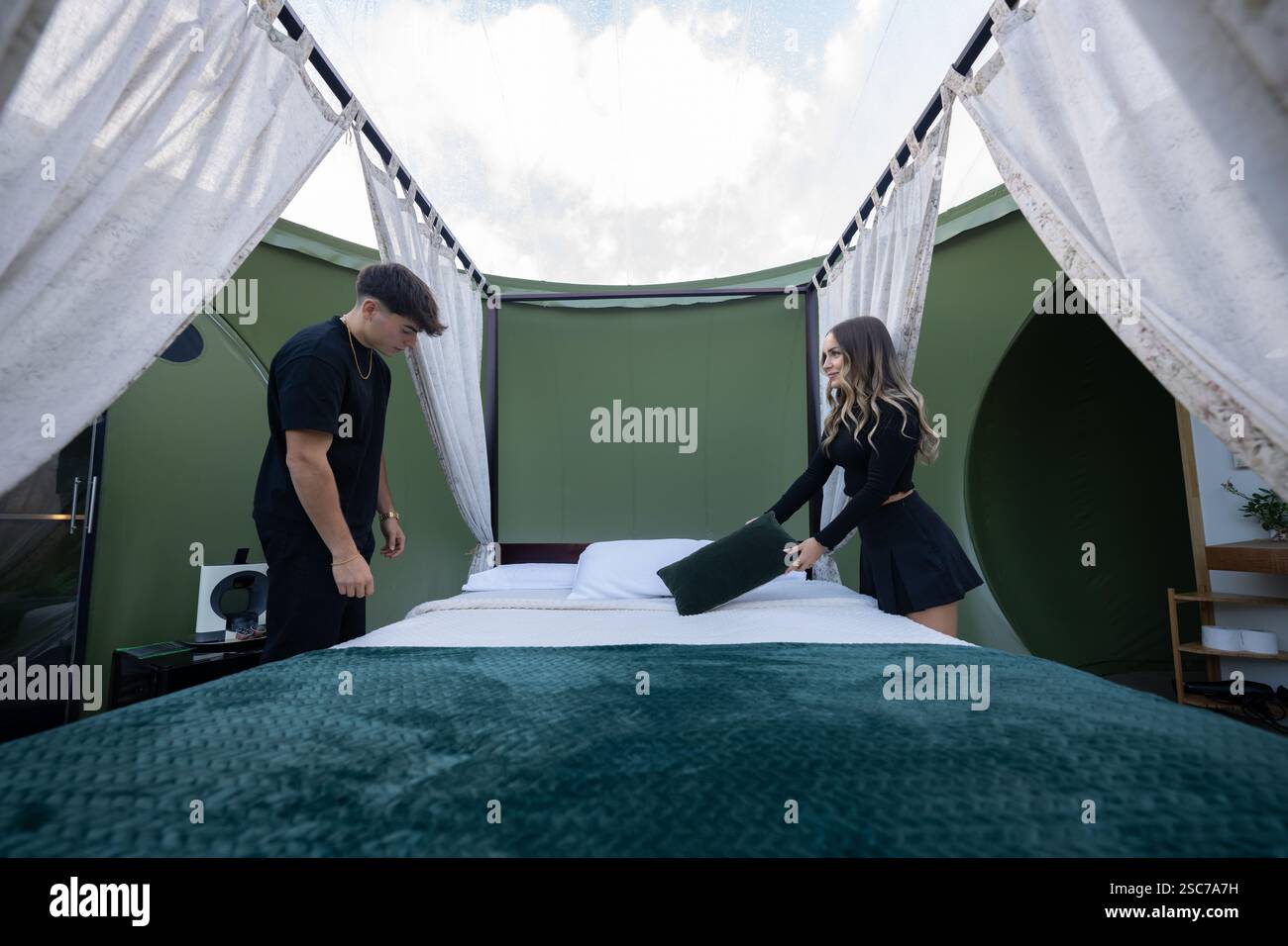 Due membri del personale dell'hotel che organizzano cuscini e creano un letto all'interno di una lussuosa cupola in vetro, assicurando che ogni dettaglio sia perfetto per il comfort degli ospiti e per il sa Foto Stock