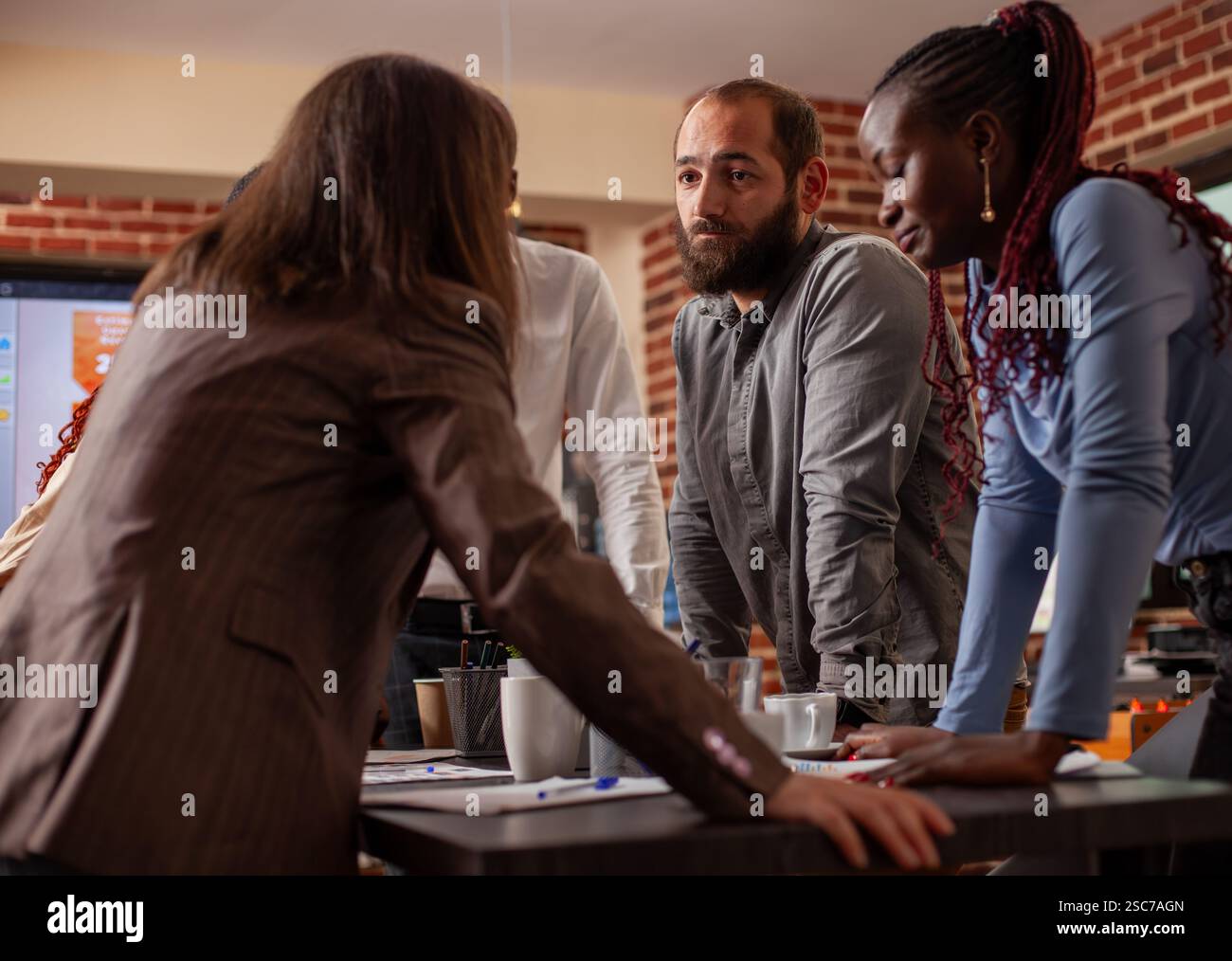 Primo piano di un team eterogeneo appoggiato al tavolo, profondamente impegnato nella discussione di importanti questioni aziendali. Collaborazione di gruppo con strumenti digitali e documenti finanziari nella sala riunioni a muro. Foto Stock