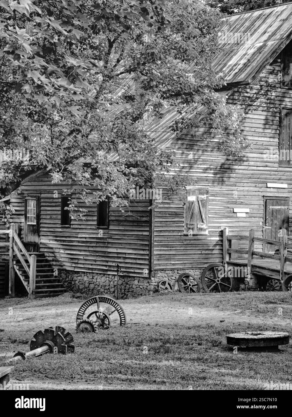 Rustico mulino in legno con ingranaggi invecchiati e esterno intempestivo, circondato da alberi. Una nostalgica scena in bianco e nero cattura l'artigianato storico. Foto Stock