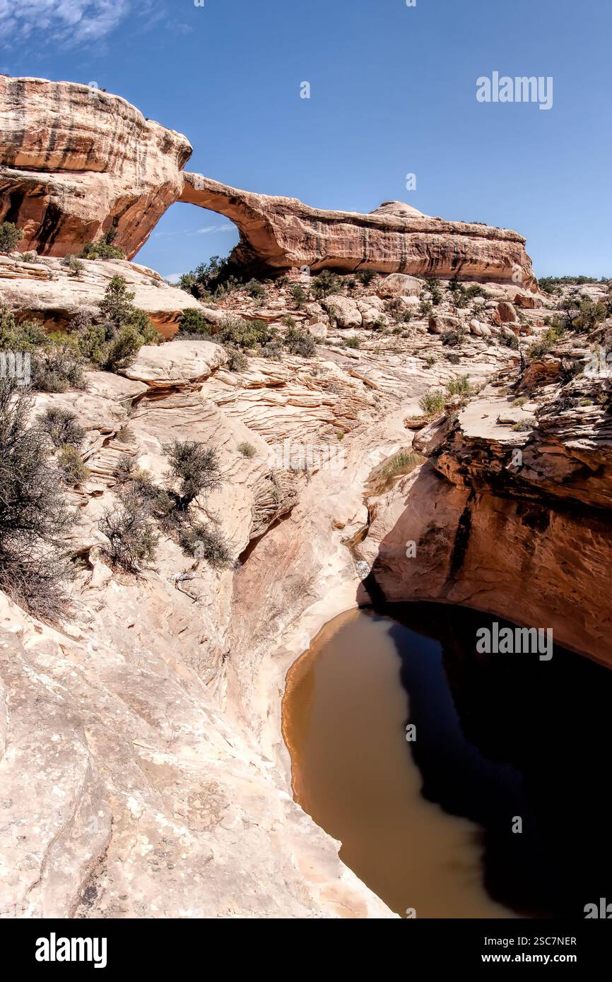 Una grande formazione rocciosa con un piccolo foro al centro. Il foro è pieno d'acqua. Il cielo è blu e limpido Foto Stock