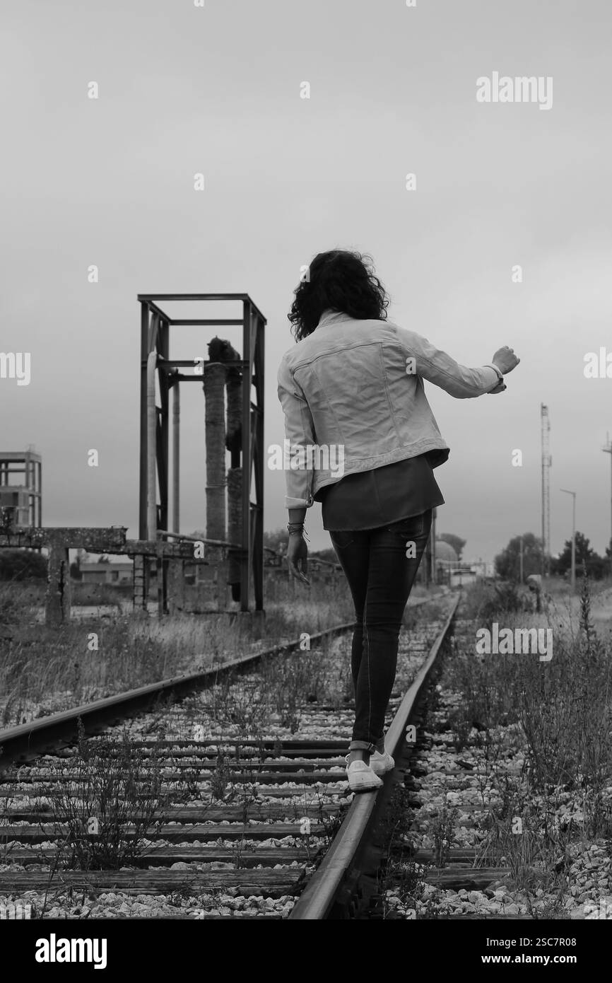 Donna non identificata da dietro che cammina sulla cima di una linea ferroviaria in una zona industriale di ​​Barreiro-Portogallo. Foto Stock