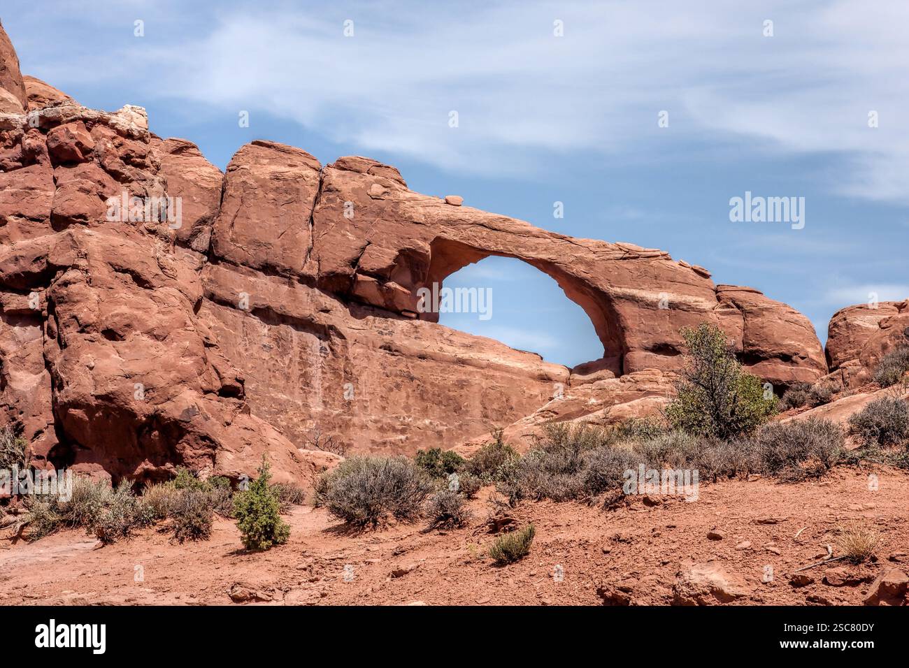 Una grande formazione rocciosa con un foro al centro. Il buco è circondato da cespugli e alberi Foto Stock