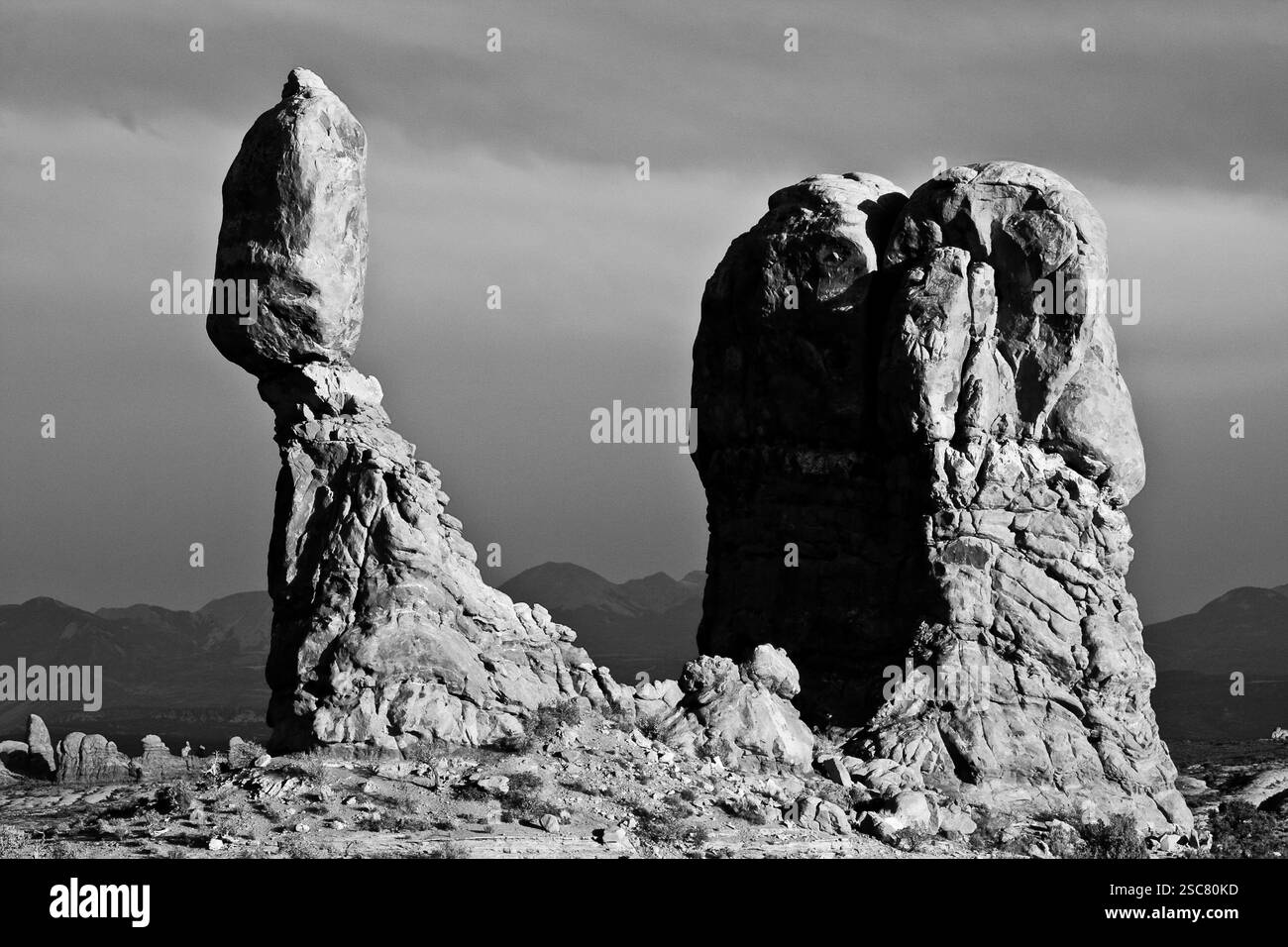 Una grande roccia si trova in cima a una roccia più piccola, creando una formazione unica e interessante. La scena si svolge in un deserto, con le rocce in piedi Foto Stock Una grande roccia si trova in cima a una roccia più piccola, creando una formazione unica e interessante. La scena si svolge in un deserto, con le rocce in piedi Foto Stock