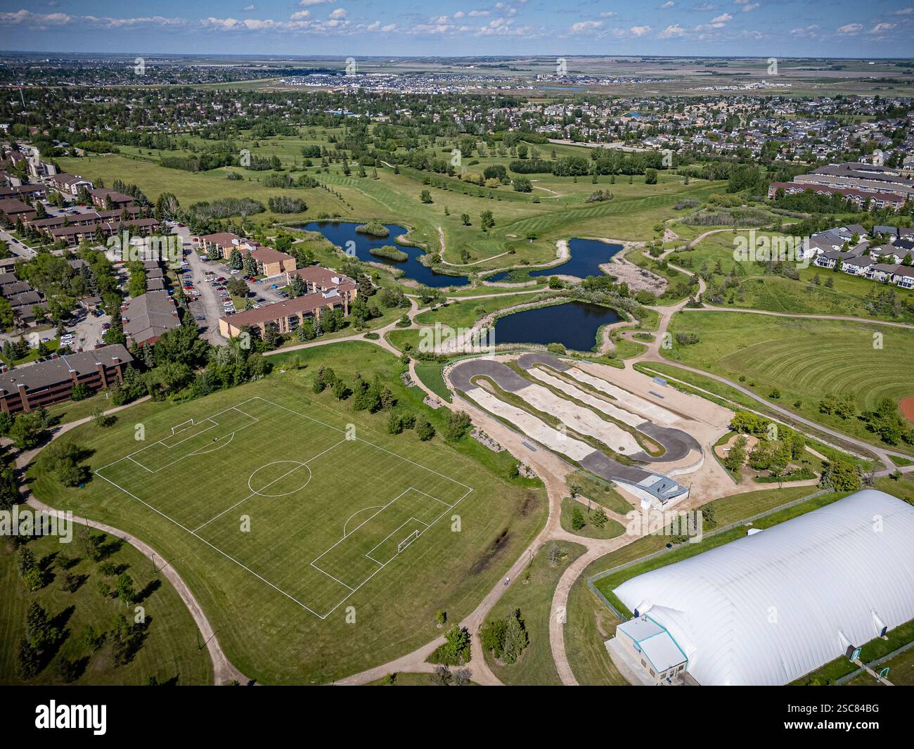 Grande campo verde con un campo da calcio al centro. Il campo è circondato da case e un campo da golf Foto Stock