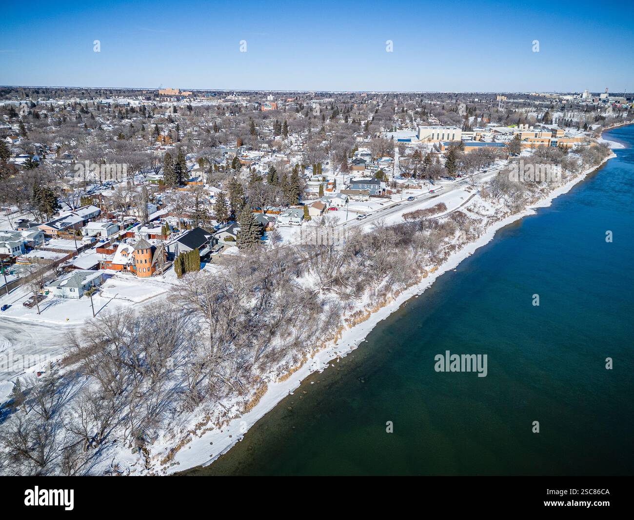 Paesaggio innevato con un fiume e case sullo sfondo. L'immagine ha un'atmosfera tranquilla e serena Foto Stock