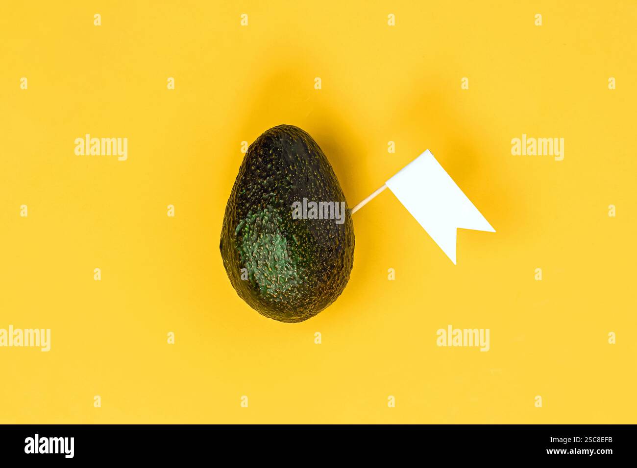 Avocado con una piccola bandiera bianca su uno sfondo giallo brillante che crea un'accattivante esposizione Foto Stock