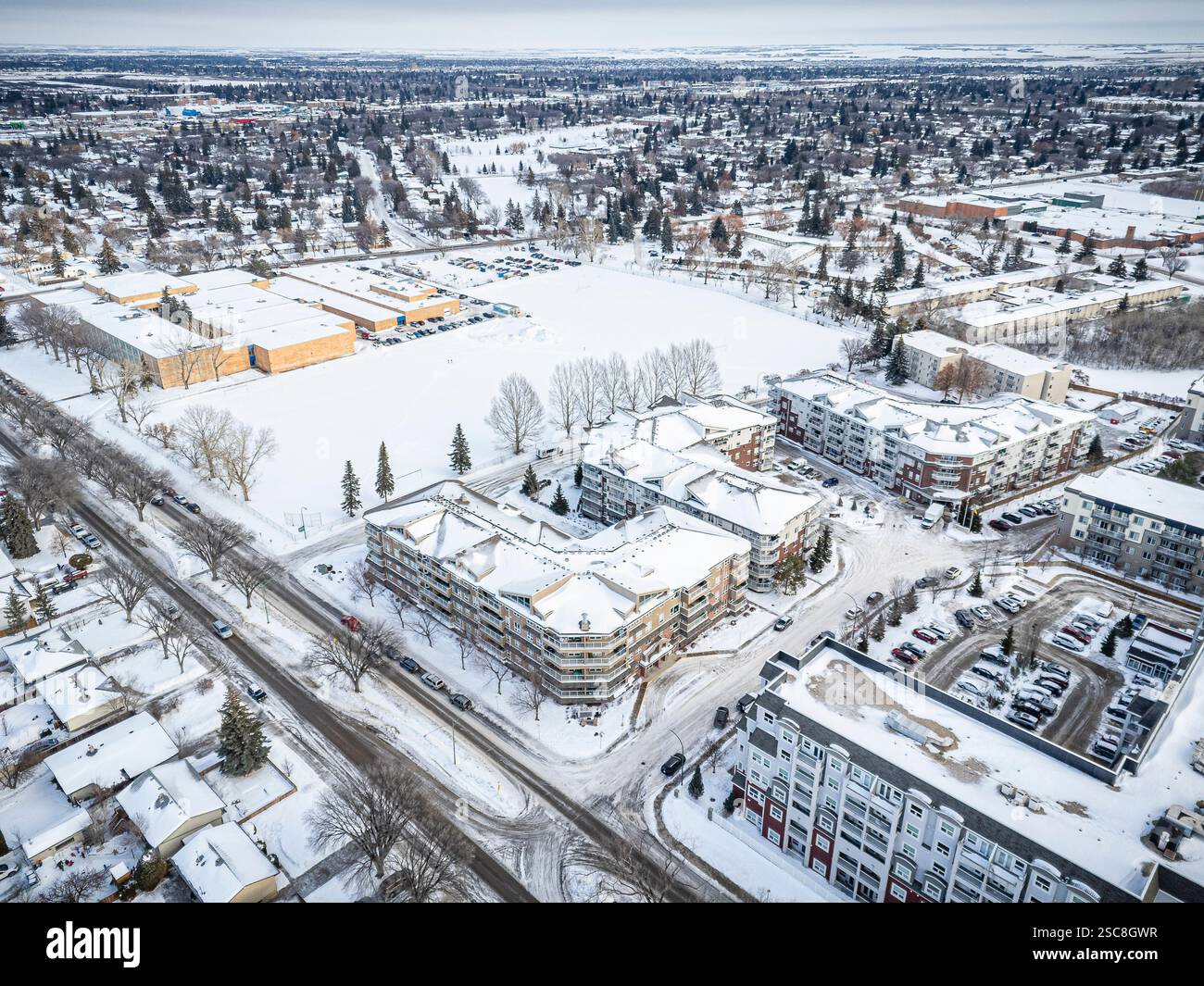 Paesaggio urbano innevato con un grande complesso di appartamenti nel centro. La neve copre il terreno e gli edifici, dando alla scena un sereno e sereno Foto Stock