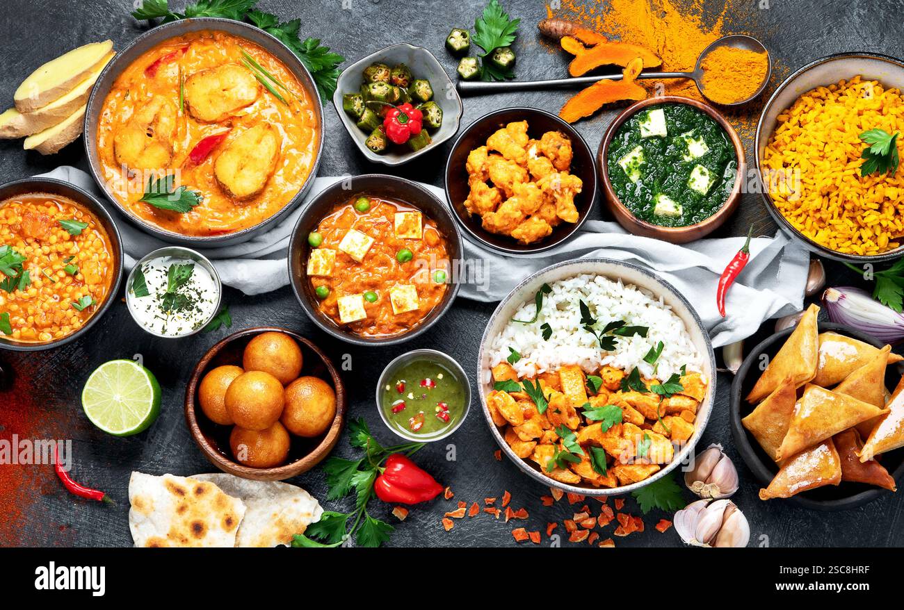 Piatti della cucina indiana. Curry, pollo al burro, riso, lenticchie, paneer, samosa, spezie. Ciotole e piatti con cibo indiano. Vista dall'alto. Foto Stock